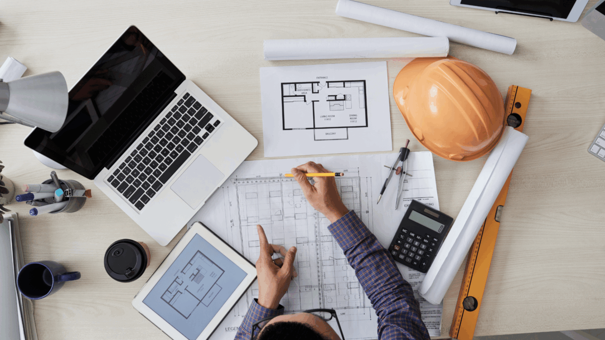 Engineer writing on building plans with tools nearby.